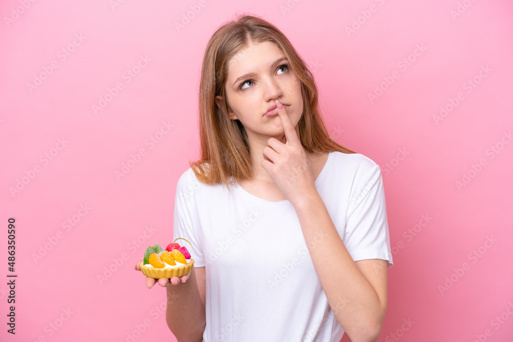 Teenager Russian girl holding a tartlet isolated on pink background having doubts while looking up Teenager Russian girl holding a tartlet isolated on pink background having doubts while looking up