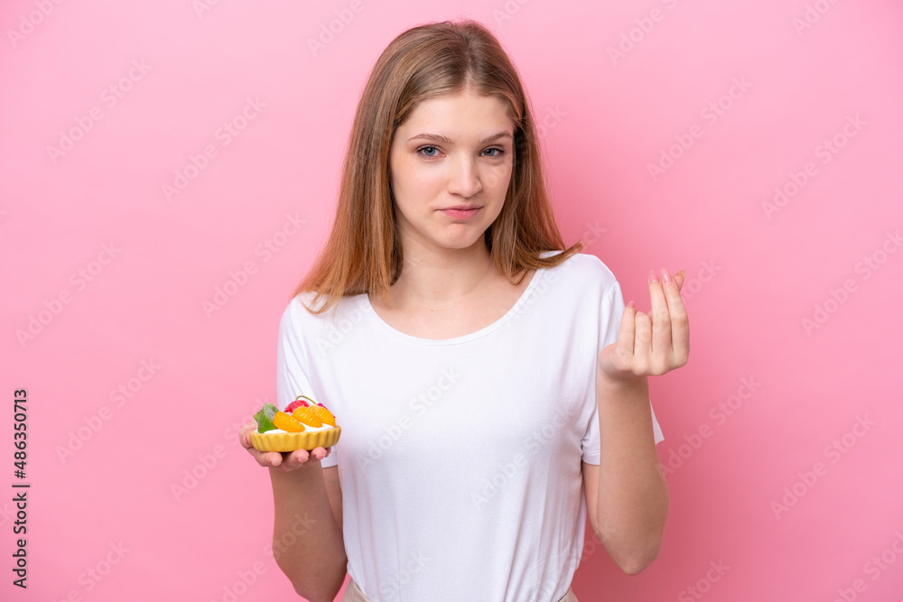 Teenager Russian girl holding a tartlet isolated on pink background making money gesture Teenager Russian girl holding a tartlet isolated on pink background making money gesture
