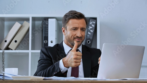 smiling businessman showing thumb up during video call on laptop