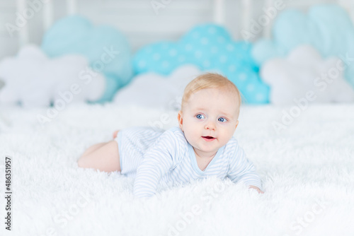 baby on the bed in blue pajamas goes to bed or wakes up in the morning, baby boy blonde six months