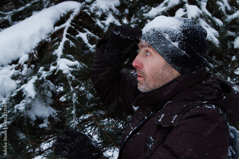 Image of a man standing sideways near the branches of a Christmas tree in the snow. Image of a man standing sideways near the branches of a Christmas tree in the snow.