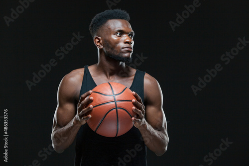 Portrait of afro american male basketball player playing with a ball over black background. Fit young man in sportswear holding basketball