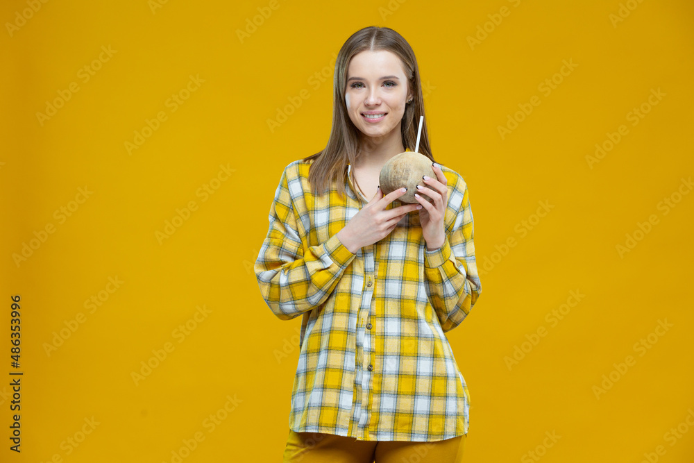 Shot of an attractive young smiling woman looking aside holding in both hands coconut with a straw isolated on yellow background. Concept of healthy lifestyle, proper nutrition, diet, vegan Shot of an attractive young smiling woman looking aside holding in both hands coconut with a straw isolated on yellow background. Concept of healthy lifestyle, proper nutrition, diet, vegan