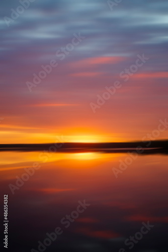 Soft and blurred beautiful sunset and colorful cloudy sky and their reflections on a lake. Artistic abstract landscape photography background with copy space.