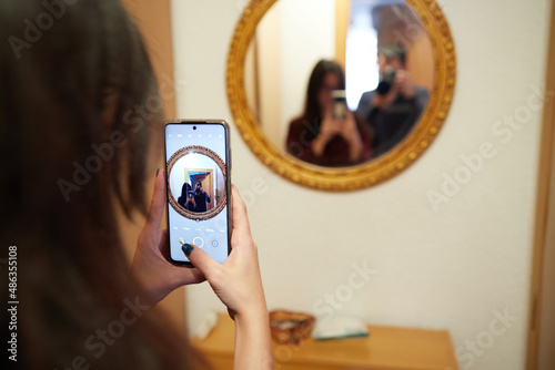 Tableau sur toile Smiling girl taking a selfie with a mirror while an anonymous boy takes her pict