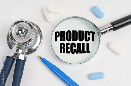 On a white surface lie pills, a pen, a stethoscope and a magnifying glass with the inscription - PRODUCT RECALL photo
