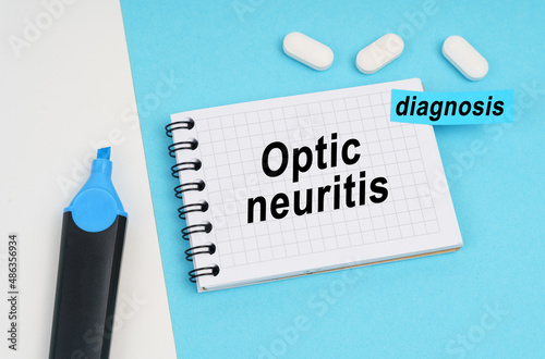 On a white and blue surface are pills, a marker and a notebook with the inscription - Optic neuritis photo