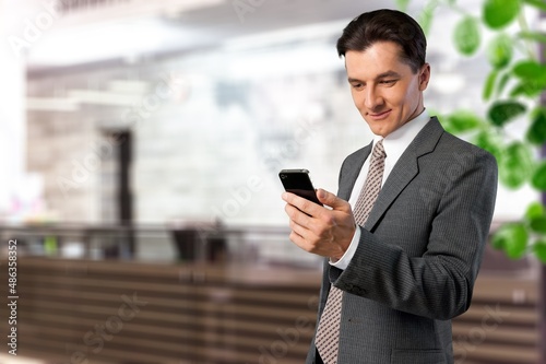 Smiling ceo businessman holding using cell phone mobile apps standing in office