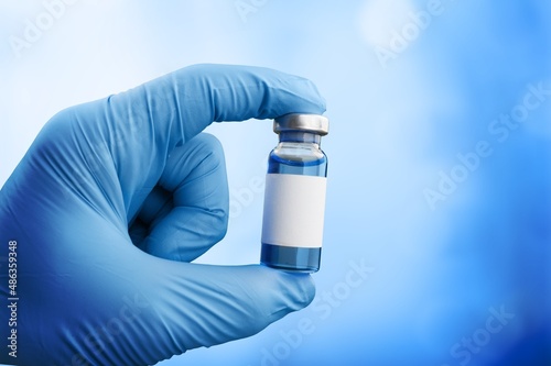 Hand in medical gloves holding a vaccine vial with Covid 19 Vaccine Booster text, for Coronavirus booster shot. photo