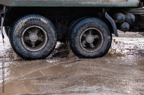 Rear wheels of a truck in muddy puddle of broken road