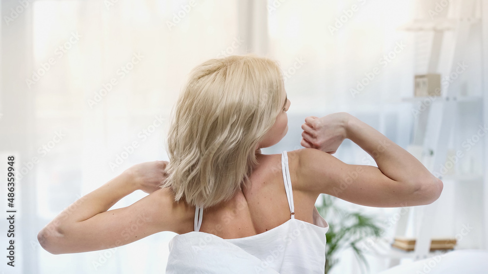 back view of young blonde woman stretching in bedroom back view of young blonde woman stretching in bedroom
