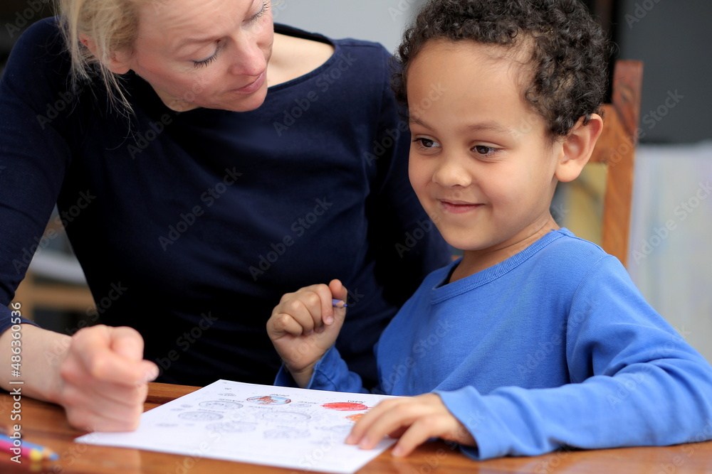 child doing homework learning at home with mother sitting at a table stock photo child doing homework learning at home with mother sitting at a table stock photo