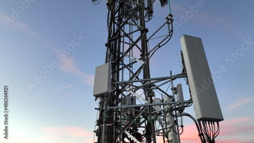 Cell tower with multiple 5G, 4G & LTE antennas and radio dishes. Close-up video from drone with tower against evening sky.