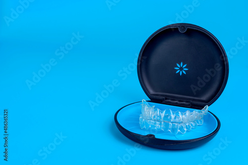 Black plastic case with transparent braces on blue background. Insivible removable retainers for orthodontic treatment photo