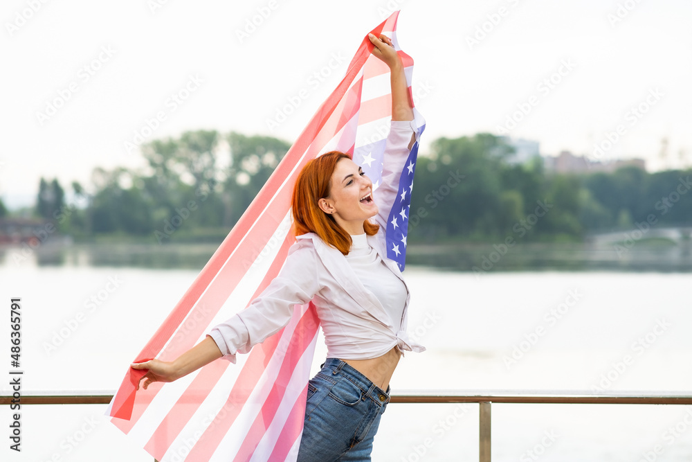 Back view of happy young woman with USA national flag on her shoulders. Positive girl celebrating United States independence day