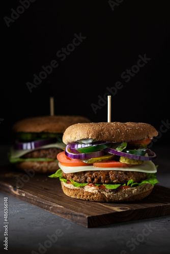 Vegan meatless burger with plant-based meat, tomatoes, papers, cheese and onion. Vertical with copy space.