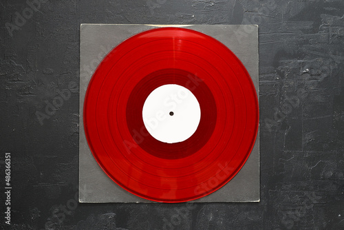 Aged black paper cover and red vinyl LP record isolated on stone background	
