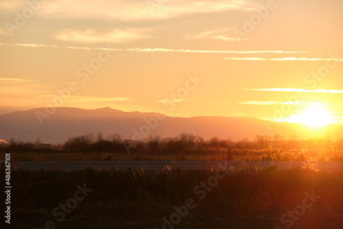 Beautiful evening panoramic landscape with bright setting sun over distant mountain peaks and asphalt road in front at sunset © bilanol