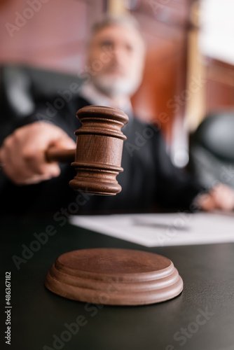 Foto selective focus of wooden gavel in hand of blurred judge in court