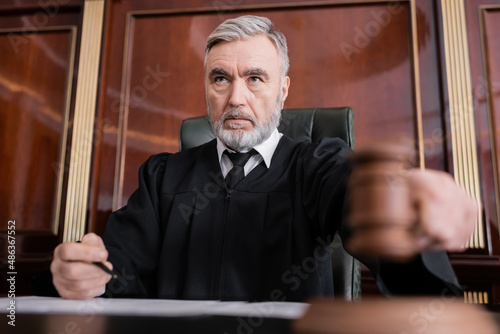 senior judge in mantle holding blurred gavel while sentencing in court photo