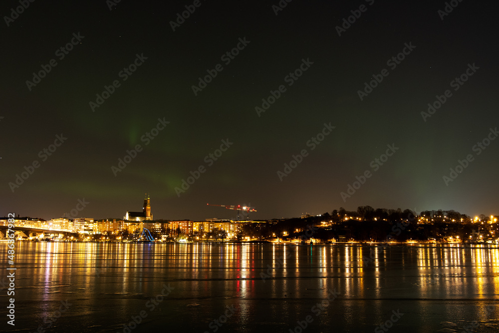 Northern lights, or Aurora Borealis, over Stockholm city skyline on a cold winter night with frozen water. Night view of Södermalm in Stockholm, Sweden. Photo taken February 10, 2022.