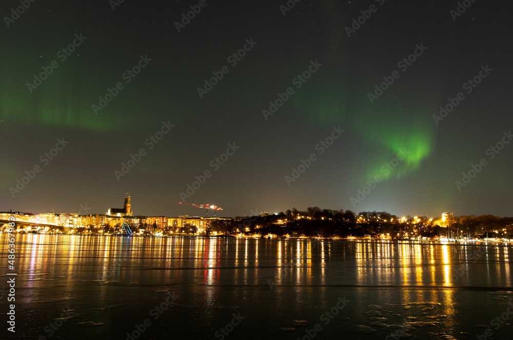Scenic northern lights, or Aurora Borealis, over Stockholm city skyline on a cold winter night with frozen water. Night view of Södermalm in Stockholm, Sweden. Photo taken February 10, 2022.