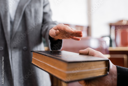 partial view of woman giving oath on holy bible in courtroom photo