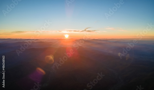 Aerial view of dark mountain hills with bright sunrays of setting sun at sunset. Hazy peaks and misty valleys in evening