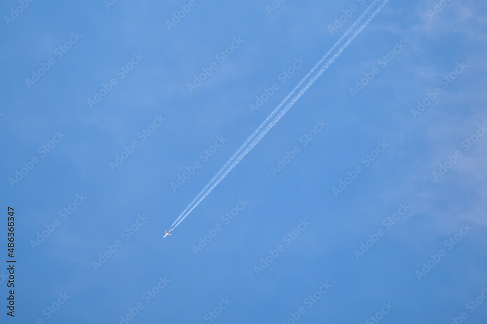 Distant passenger jet plane flying on high altitude on clear blue sky leaving white smoke trace of contrail behind. Air transportation concept Distant passenger jet plane flying on high altitude on clear blue sky leaving white smoke trace of contrail behind. Air transportation concept