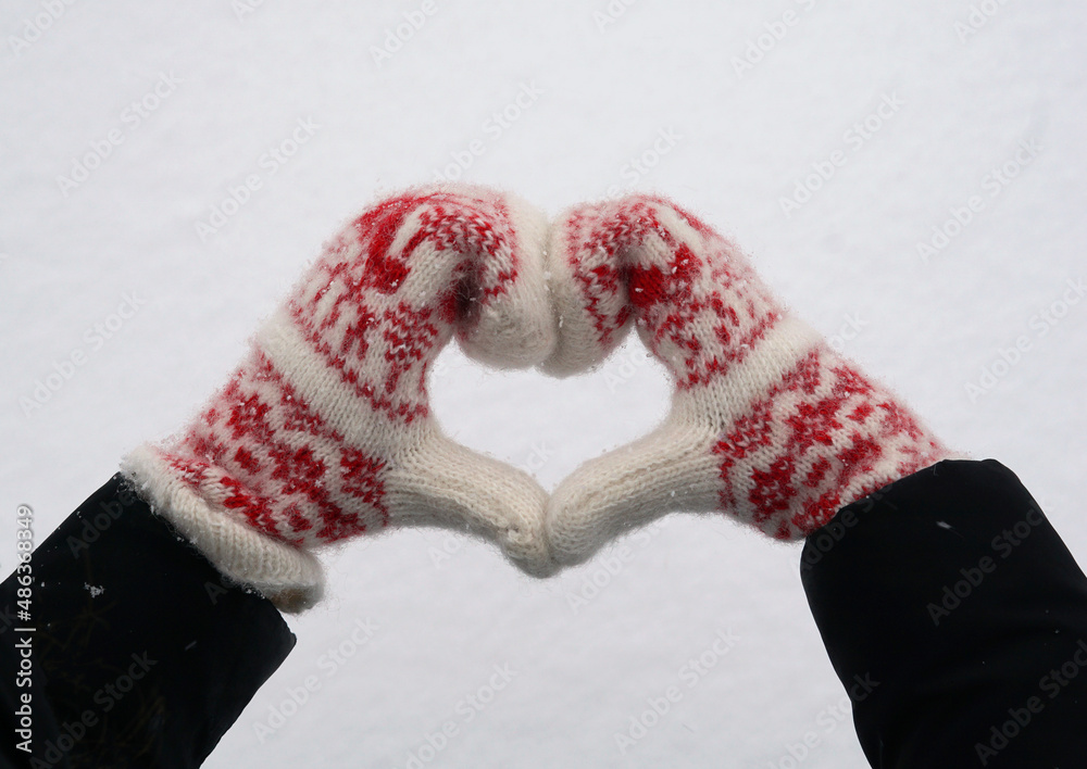 Women's hands in white and red mittens in the shape of Heart on the snow