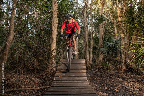 Obraz na płótnie man riding a mountain bike on a trail with wood features w salonie