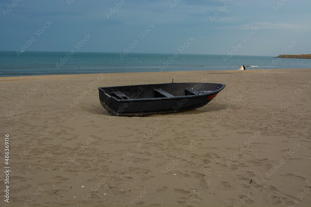 black boat on beach,people sitting in background.Solitude,friendship,sunset and vacation photo.