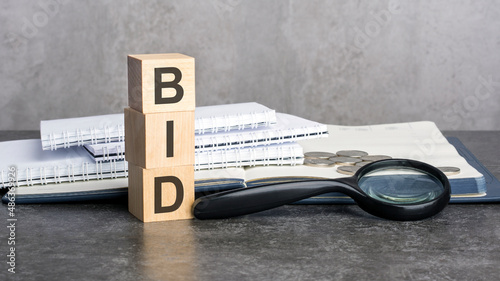 the word BID is written on wooden cubes on a gray background. close-up of wooden elements, magnifying glass, paper documents photo