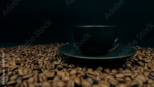 a cup of espresso on a black background and roasted coffee beans underneath. Background concept