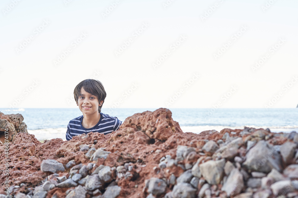 The boy looking at camera, sitting on a rock by the sea.