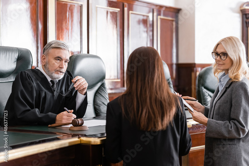 Tableau sur toile thoughtful judge holding eyeglasses listen to prosecutor standing near attorney