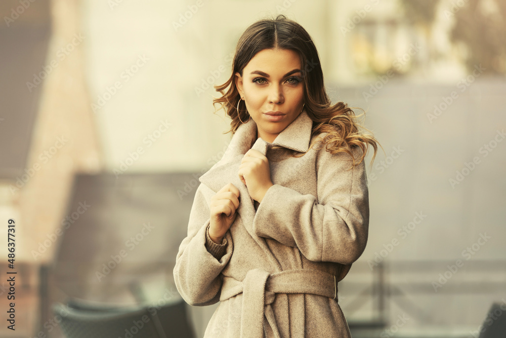 Young woman with long curly hairs in light beige coat