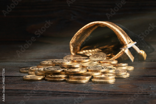 A bag with gold coins on a wooden background. The money in a black bag on a wooden table. Treasure Hunt. A Purse with money. Wallet wit gold coins.