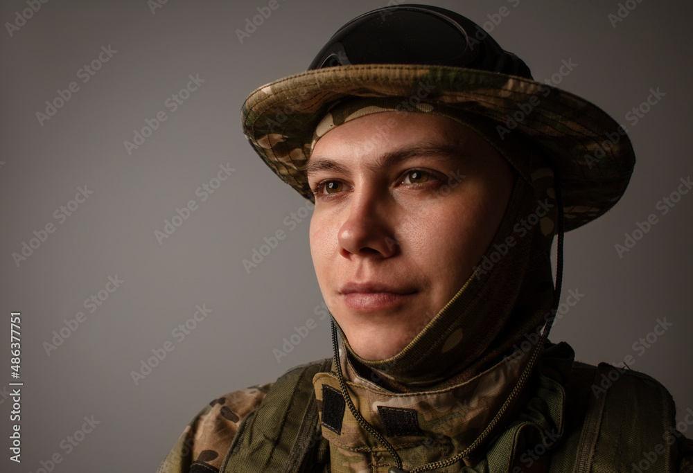A close-up shot of a military man in a uniform in a hat with goggles giving orders on the grey background. Portrait of the soldier . Calm warrior. Army.
