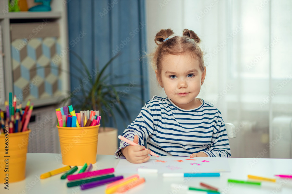 A beautiful little girl sits at a table at home and draws. Development of preschoolers. A beautiful little girl sits at a table at home and draws. Development of preschoolers.