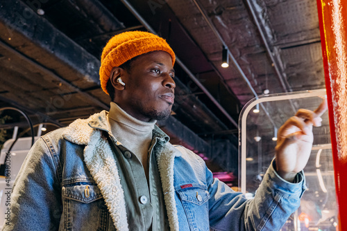 Photography Positive African-American guy in orange knitted hat with wireless earphones orde