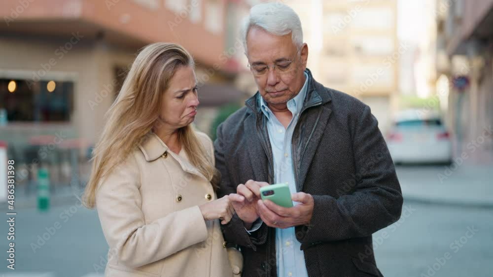 Middle age couple couple with cheerful expression using smartphone at street Middle age couple couple with cheerful expression using smartphone at street