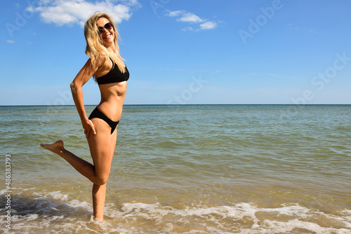 Young beautiful blonde woman of white race posing on the beach in a swimsuit near the sea and smiling