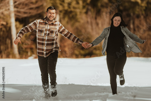 Couple running and holding hands in the winter snowy forest. Selective focus photo