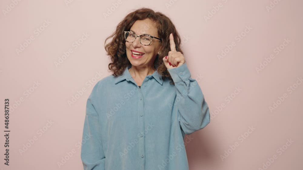 Middle age woman smiling confident doing idea gesture with finger over pink background Middle age woman smiling confident doing idea gesture with finger over pink background
