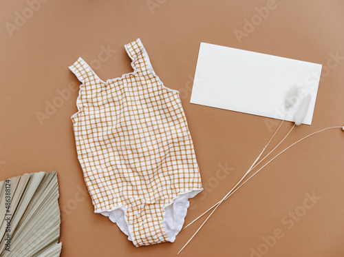 Cute retro swimsuit for baby girl on brown background. Summer holiday concept. Top view, flat lay photo