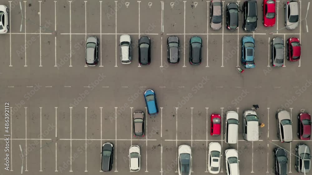 Blue car pulls out of the parking lot. Car leaves the parking lot - an aerial top overhead view. Parking with many places near the supermarket - overhead view. Blue car pulls out of the parking lot. Car leaves the parking lot - an aerial top overhead view. Parking with many places near the supermarket - overhead view.