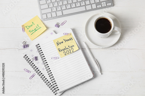 Cup of coffee, computer keyboard, stationery, sticky notes with text NEW YEAR'S RESOLUTION 2022 and DON'T FORGET on white wooden background