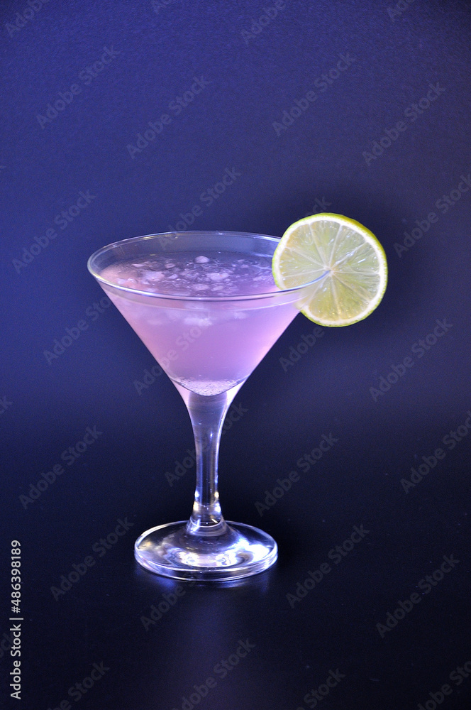 Cosmopolitan cocktail, conical glass with finely chopped ice and a slice of lemon on a black background.