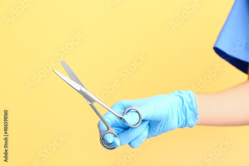 Female doctor with medical scissors on yellow background